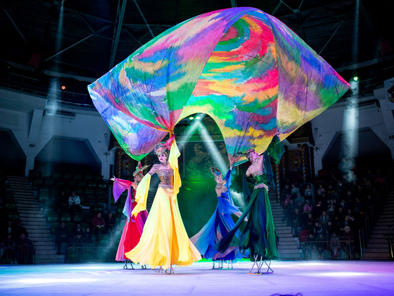 Four girls on ice stilts hold a large colorful cloth above their heads. Moscow circus on ice